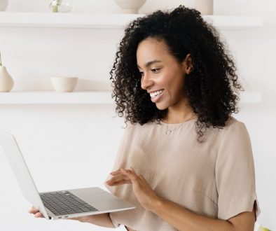A women is smiling while she looks into the laptop she is holding