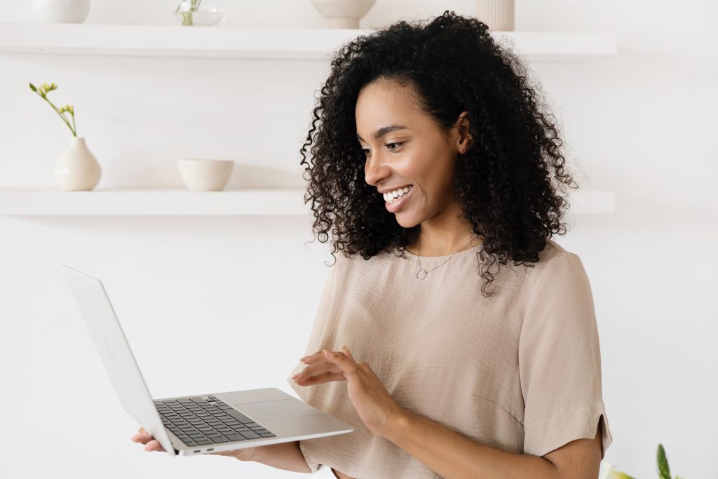 A women is smiling while she looks into the laptop she is holding